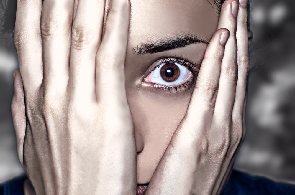 A dramatic image of a person that just misspoke in the audit room. Her image shows the concept of anxiety and fear with an intense look through her hands partially covering her face.