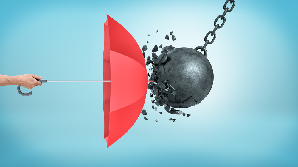 A hand holding an open red umbrella which protects from a collision with a broken wrecking ball. A representation of what patent protection can do for your medical device.